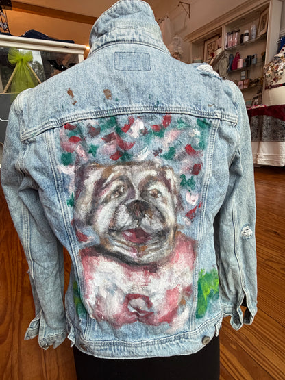 Back of a distressed light wash denim jacket with a hand-painted Georgia Bulldog in a red jersey.
