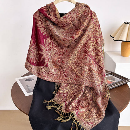Red and gold patterned woven wrap draped over black fabric on a hanger, showing fringed ends.