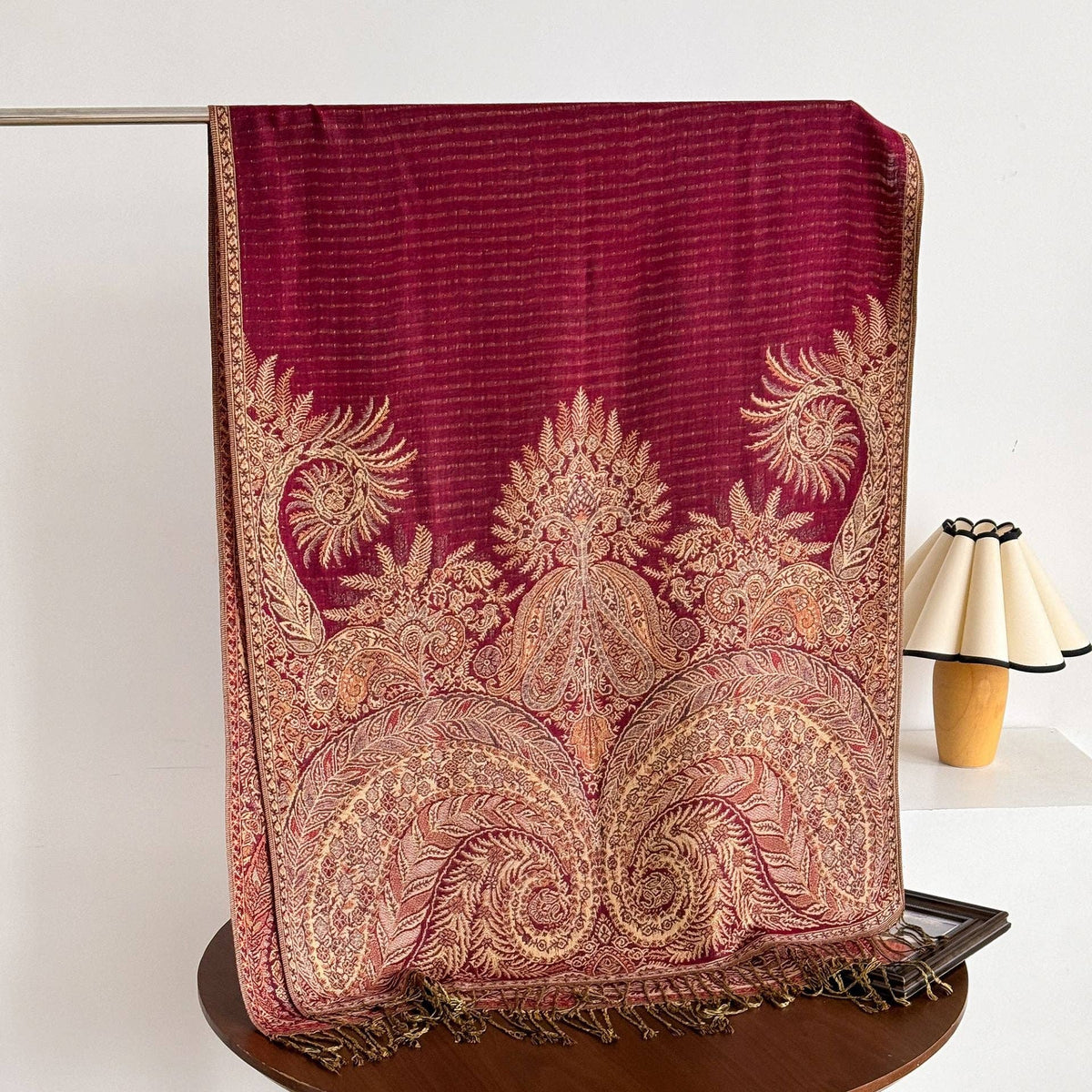 Hanging red heritage-print wrap showing detailed gold paisley motifs and twisted fringe.