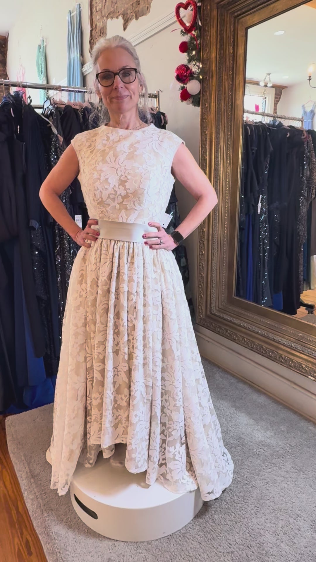 Woman in a lace dress standing in a clothing store with a large mirror.
