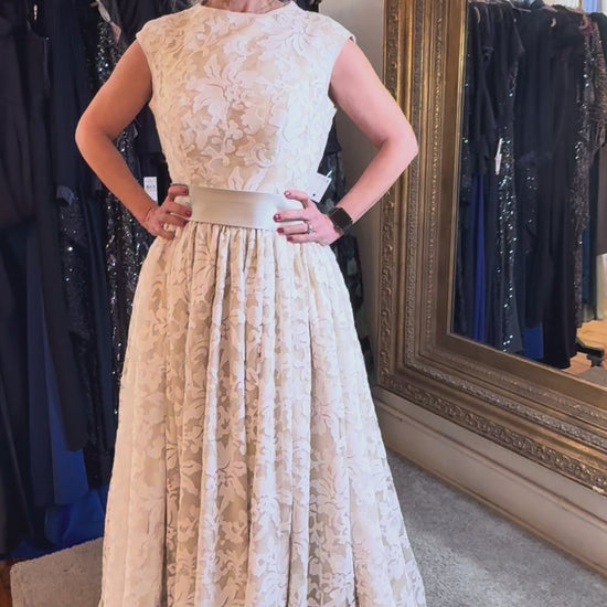 Woman in a lace dress standing in a clothing store with a large mirror.