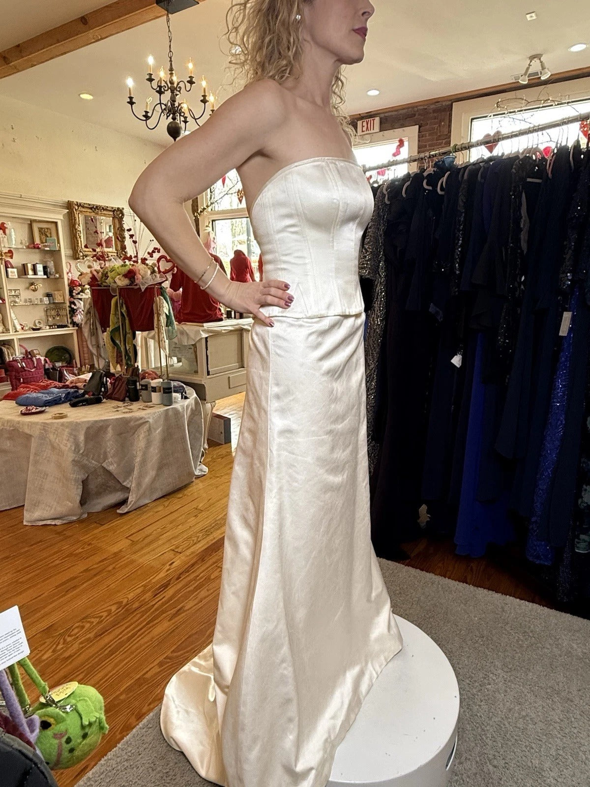 Woman wearing a white strapless gown in a store setting with racks of dresses in the background.