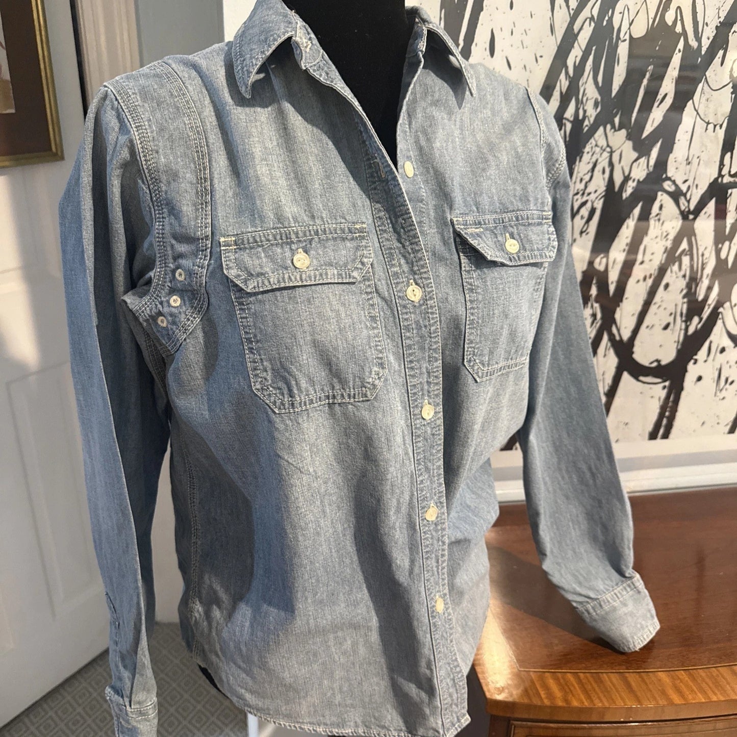 Blue denim shirt on a mannequin against a wall with abstract art