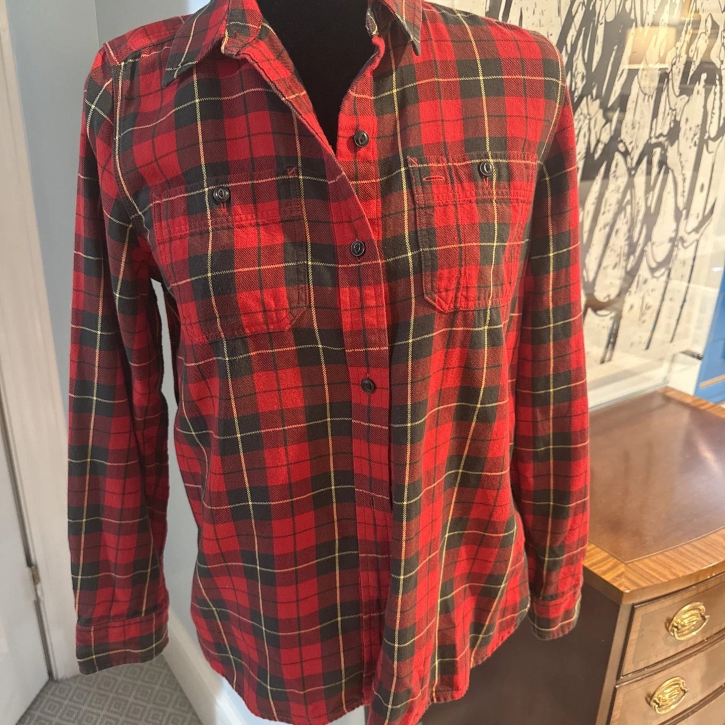 Red and black plaid shirt on a mannequin against a wall with graffiti.