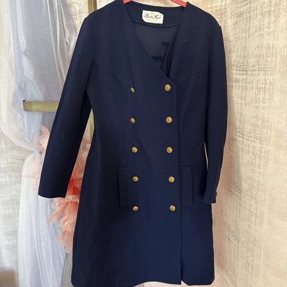 Navy blue coat with gold buttons on a hanger against a neutral wall.