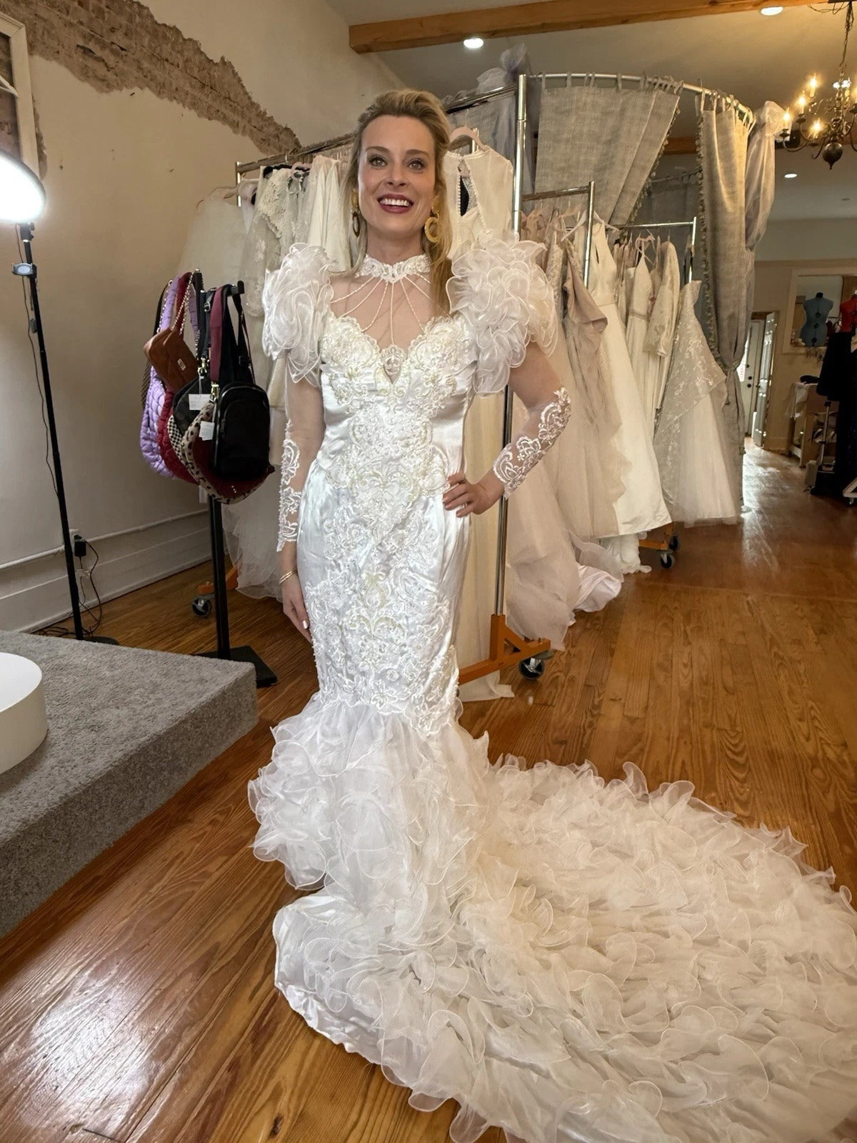 Woman in a white wedding dress standing in a bridal shop with dresses on racks in the background.