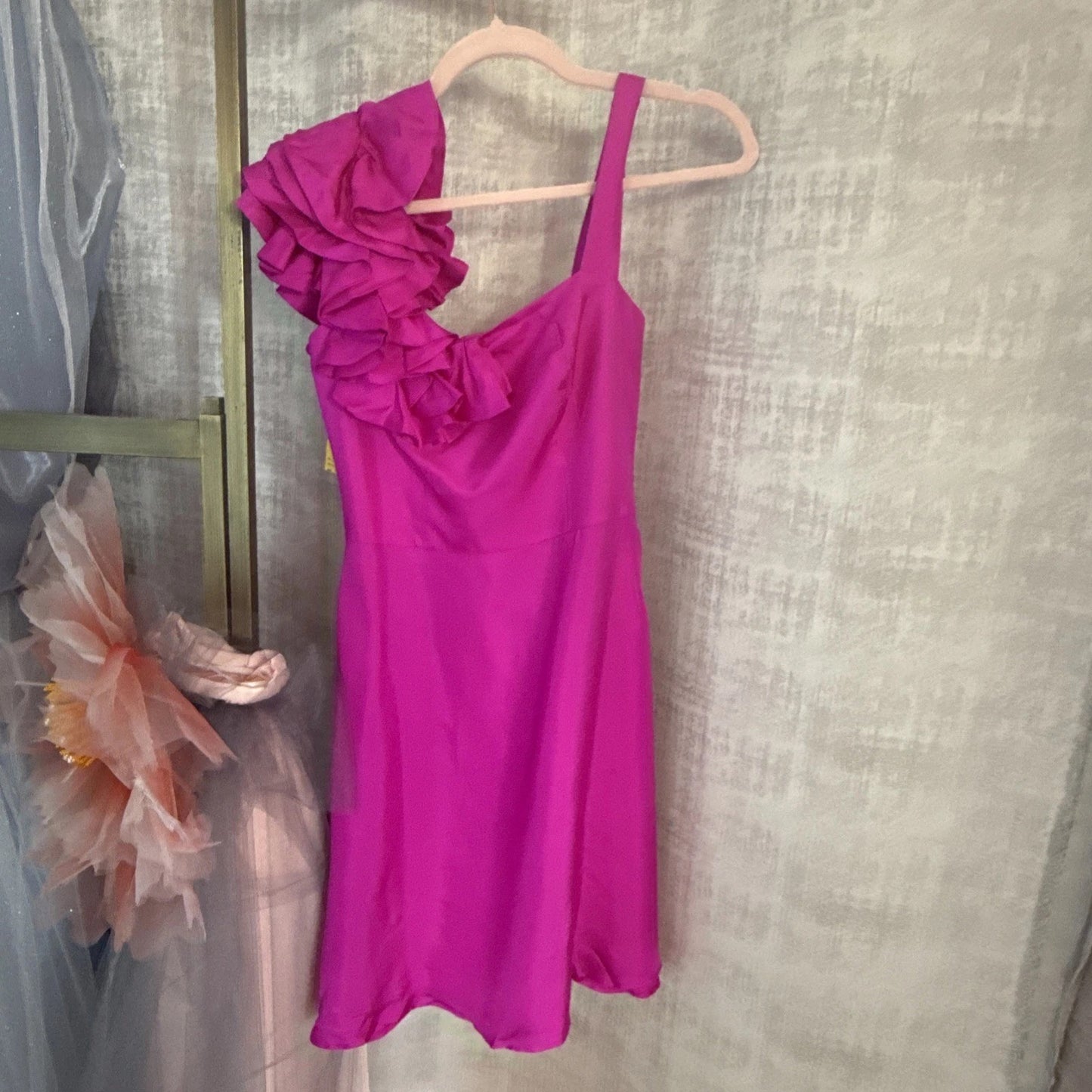 Pink dress with ruffled details on a hanger against a textured wall.