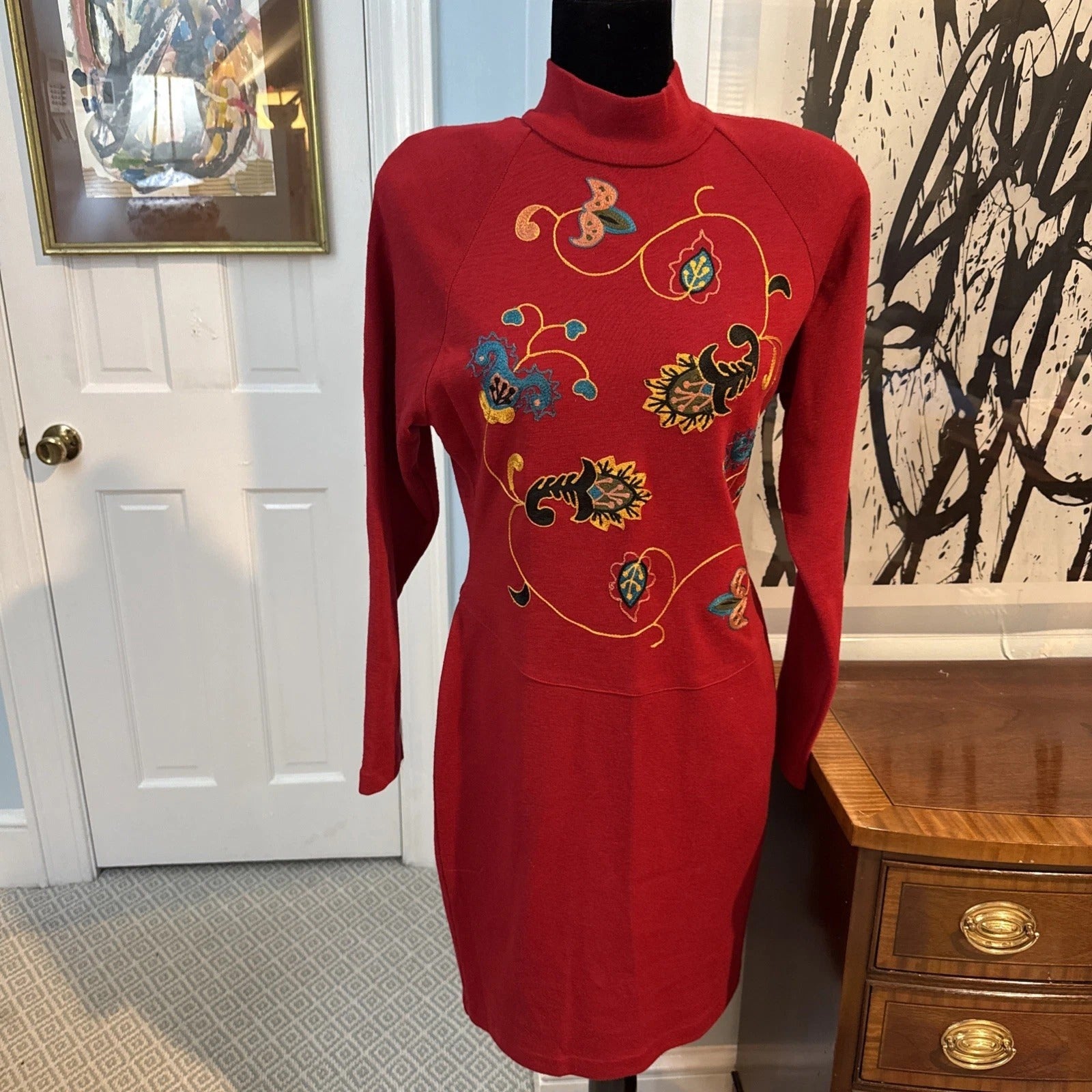 Red dress with floral embroidery on a mannequin in a room with a door and artwork.