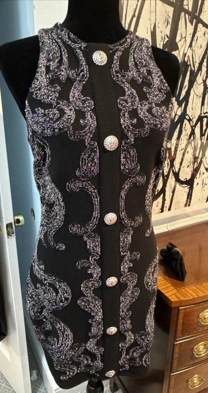 Black dress with silver lace and buttons on a mannequin against a wall.