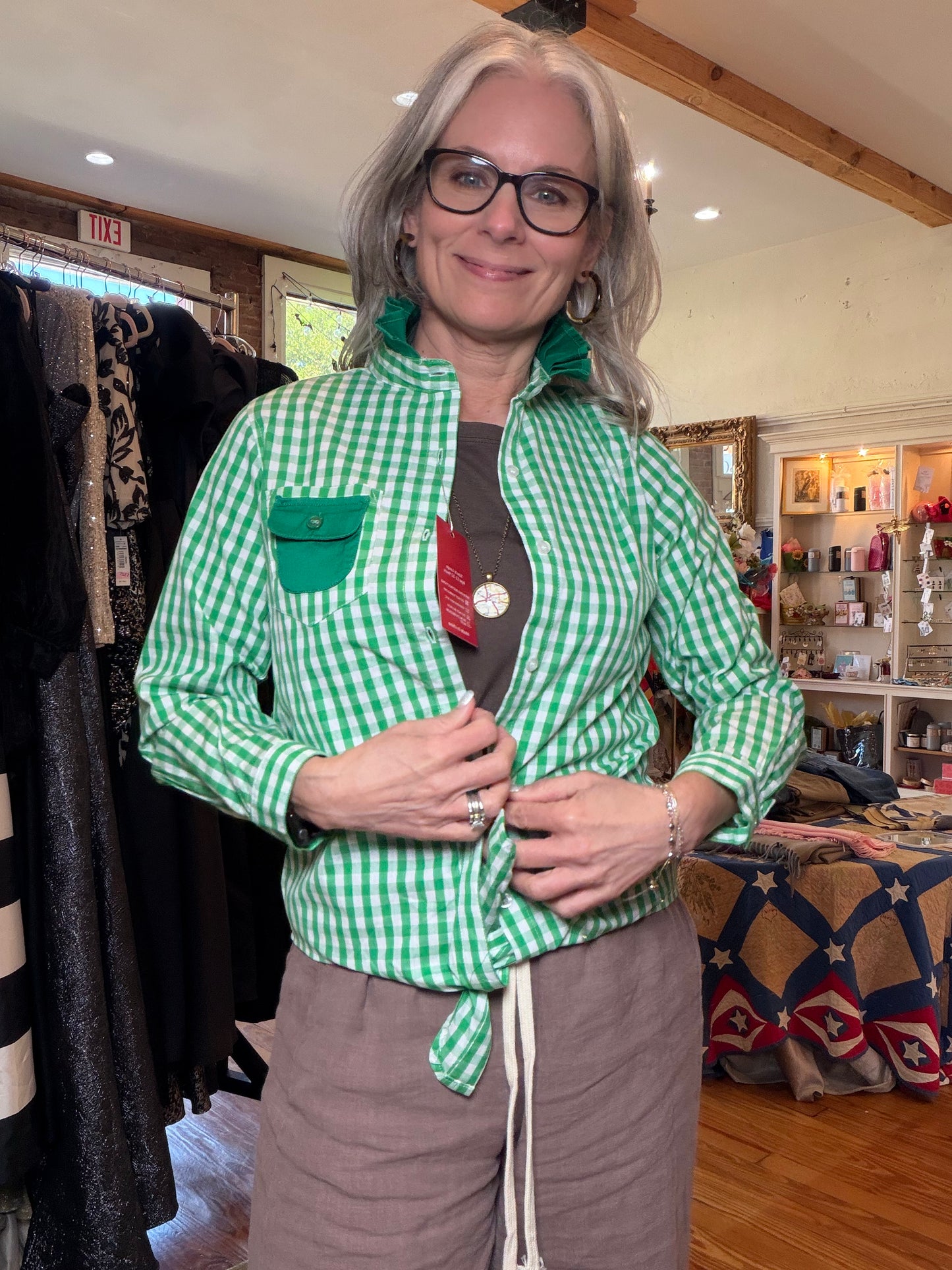 Front view of an open green gingham shirt with long sleeves, a ruffle collar and green pocket.