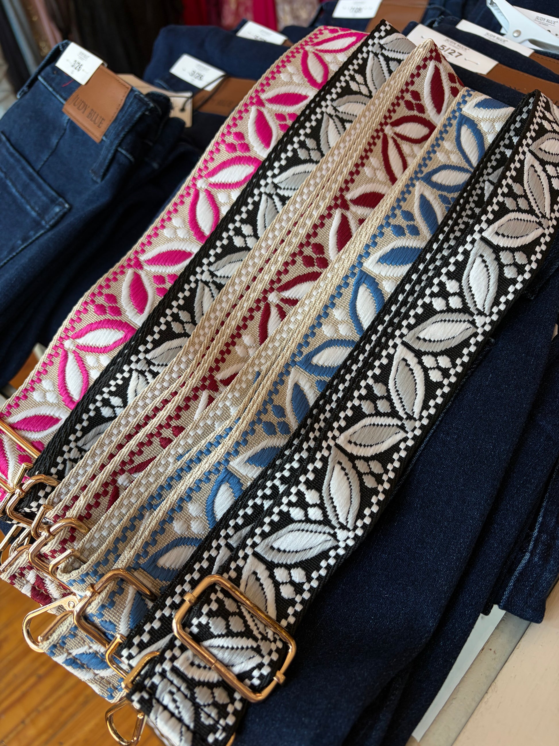 Four woven bag straps in different colors with gold-tone hardware at Dover Grace Boutique.